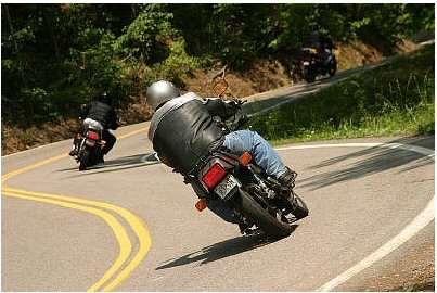 1985 Ford Crown Victoria LTD - Riders navigate a sharp turn on a scenic route, with another motorcycle visible further up the road.