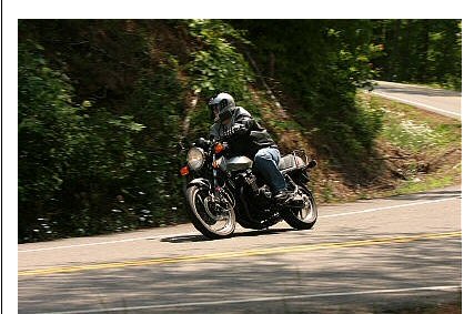 1985 Ford Crown Victoria LTD - A motorcycle rider navigates a curve on a tree-lined road.