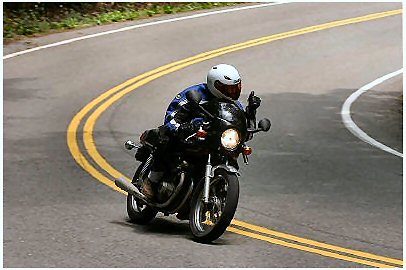 1985 Ford Crown Victoria LTD - A motorcyclist navigates a winding road, giving a thumbs-up gesture to the camera.