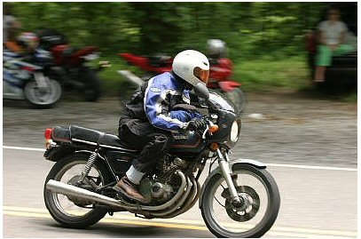 1985 Ford Crown Victoria LTD - A motorcycle rider navigates a road with other vehicles blurred in the background.