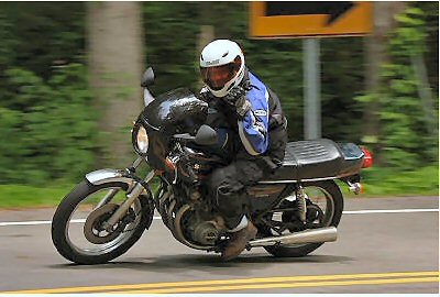 1985 Ford Crown Victoria LTD - A rider on a motorcycle navigates a tree-lined road.