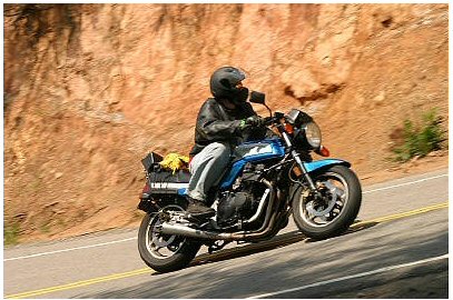 1985 Ford Crown Victoria LTD - Rider on a blue motorcycle navigates a winding road with a steep, rocky embankment.