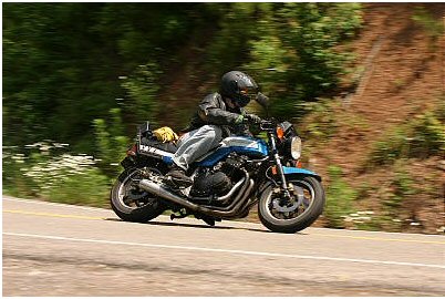 1985 Ford Crown Victoria LTD - A rider navigates a curve on a blue motorcycle, with lush green foliage lining the road.