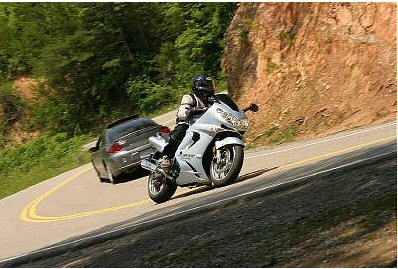 1985 Ford Crown Victoria LTD - Motorcycle navigating a curve on a scenic road, with a car following closely.