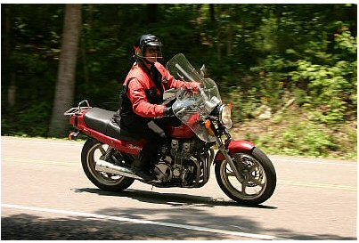1985 Ford LTD Crown Victoria - Rider on a red motorcycle navigates a tree-lined road.