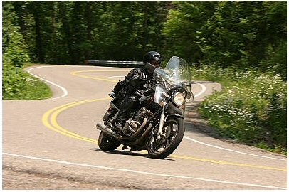 1985 Ford LTD Crown Victoria - A rider navigates a winding road through a wooded area.