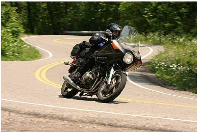1985 Ford LTD Crown Victoria - Motorcyclist navigates a sharp turn on a scenic road, leaning into the curve.