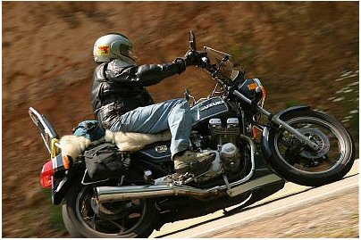 1985 Ford LTD Crown Victoria - A motorcyclist rides along a winding road, with the Suzuki logo visible on the fuel tank.
