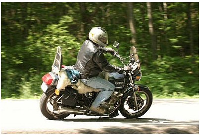 1985 Ford LTD Crown Victoria - A rider on a Suzuki motorcycle travels down a road flanked by trees.