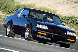 1990 Ford Bronco - A black coupe is shown driving on a road. The vehicle has a distinctive body style from the 1980s.