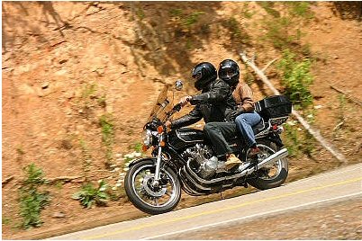 1985 Ford LTD Crown Victoria - Two people ride a motorcycle on a winding road with a rocky hillside beside them.