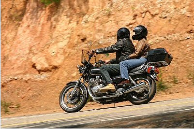 1985 Ford LTD Crown Victoria - Two people ride a motorcycle on a winding road next to a rocky hillside.