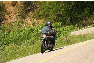 1985 Ford LTD Crown Victoria - A motorcycle rider navigates a curve on a scenic road.