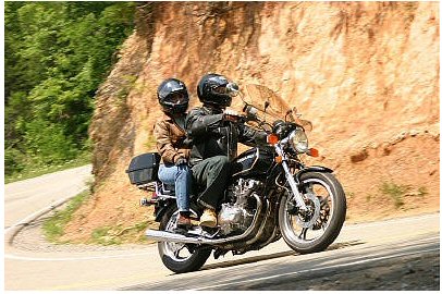 1985 Ford LTD Crown Victoria - Two people ride a motorcycle on a scenic road with a cliff face.