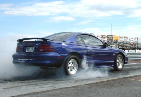 1990 Ford Bronco - A blue Ford Mustang GT performs a burnout on a drag strip, generating a large cloud of smoke.