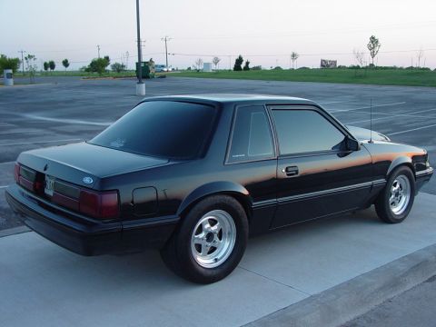 1990 Ford Bronco - A black coupe car with aftermarket wheels is parked in an empty lot.