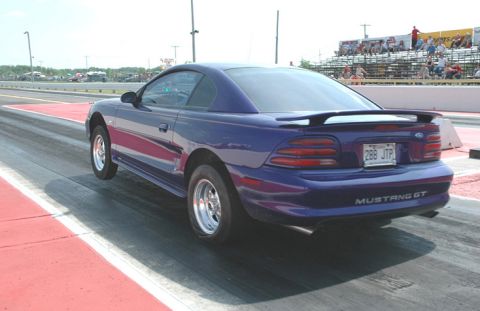 1990 Ford Bronco - A purple Ford Mustang GT is on a drag strip, viewed from the rear with a spoiler and custom wheels.