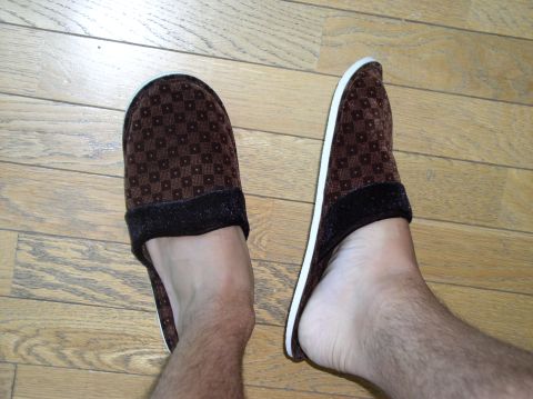 1990 Ford Bronco - A pair of brown patterned slippers are worn on feet against a wooden floor background.