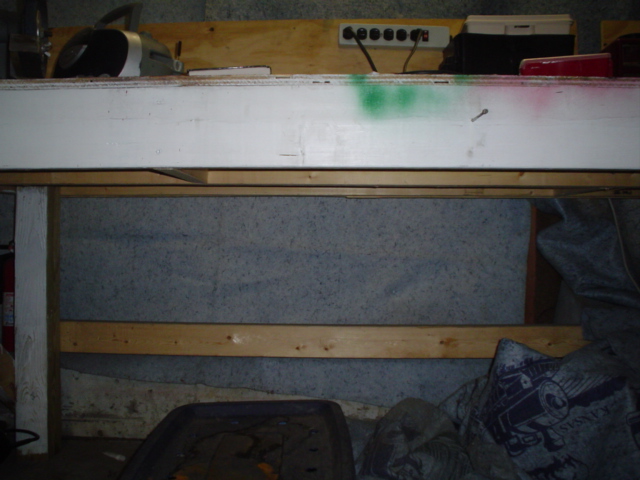 Long white panel or sheet leaning against a workbench wall in a cluttered garage