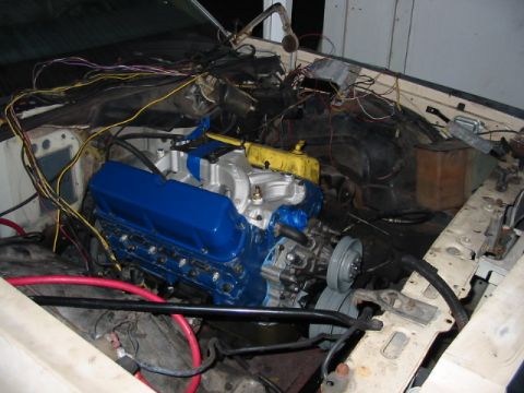 1985 Ford LTD Crown Victoria - The engine bay of a vehicle, showing a blue engine with extensive wiring and plumbing, suggesting ongoing maintenance or modification.