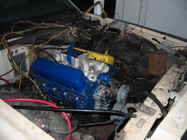 Engine bay with a blue engine, red cables, and complex wiring. The vehicle appears to be under repair