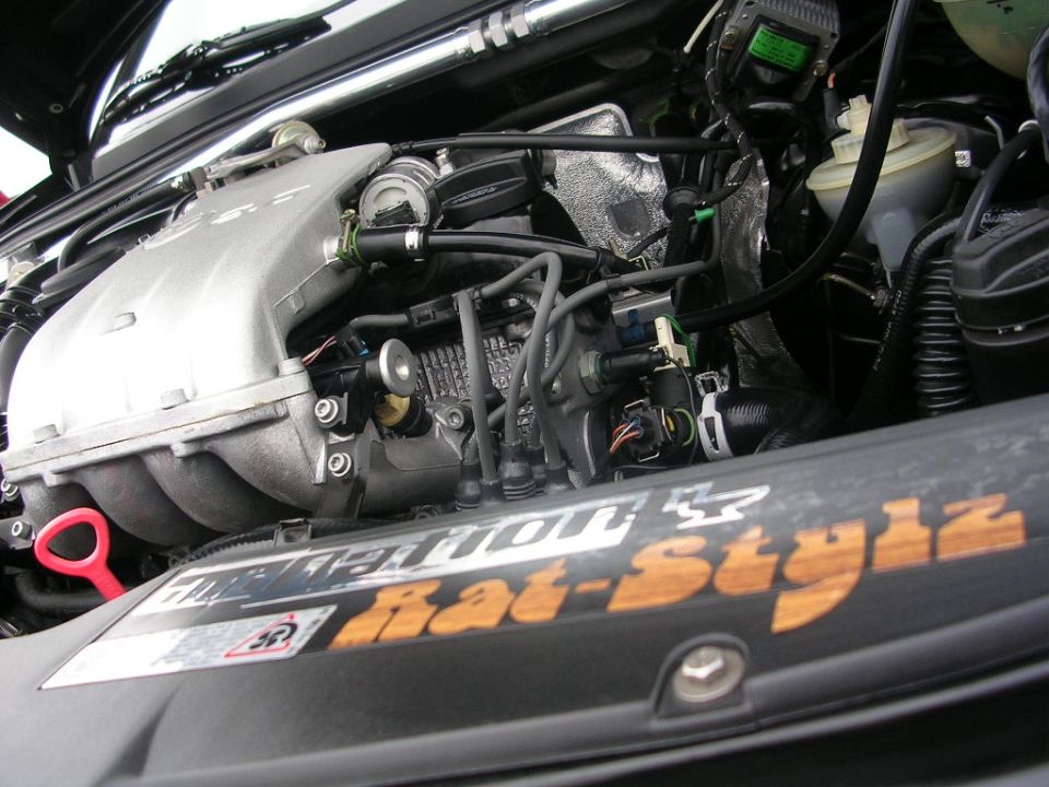 Engine bay with silver intake manifold, spark plug wires, and a sticker reading "Rat-Stylz"