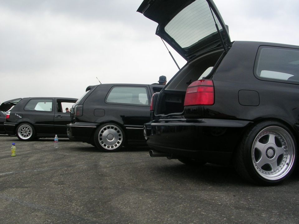 Three black hatchbacks parked on asphalt, two with open trunks
