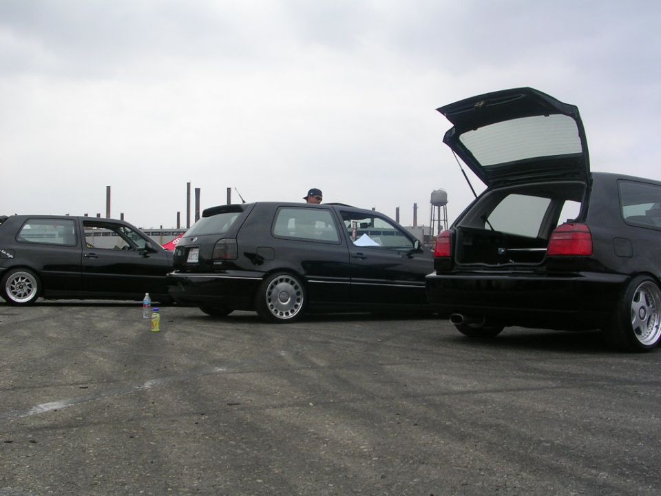 Three black hatchbacks parked outside, one with its trunk open