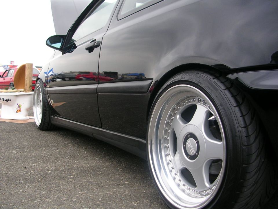 side view of black hatchback with custom wheels, red car in background