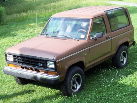 1986 Ford Bronco II - A brown 1986 Ford Bronco II is shown from the front-left angle, parked outdoors on a grassy area.