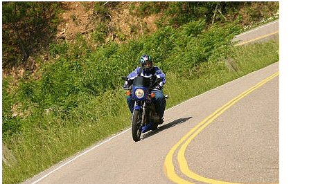 1985 Ford LTD Crown Victoria - A motorcyclist navigates a scenic, winding road on a sunny day.