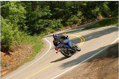 1985 Ford LTD Crown Victoria - Rider navigates a challenging curve on a scenic road surrounded by trees.