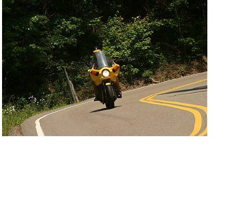 1985 Ford LTD Crown Victoria - A yellow motorcycle navigates a curve on a scenic road, indicated by double yellow lines.