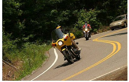 1985 Ford LTD Crown Victoria - Motorcycles navigate a winding mountain road, with a car following behind.
