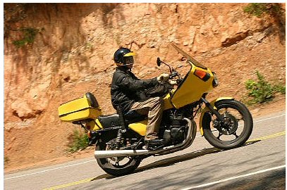 1985 Ford LTD Crown Victoria - A rider on a yellow motorcycle navigates a winding road beside a rocky embankment.