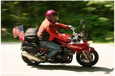 1985 Ford LTD Crown Victoria - Rider on a red motorcycle with saddlebags and an American flag waves as they ride.