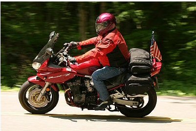 1985 Ford LTD Crown Victoria - A motorcycle rider cruises down a tree-lined road with an American flag attached to the back.