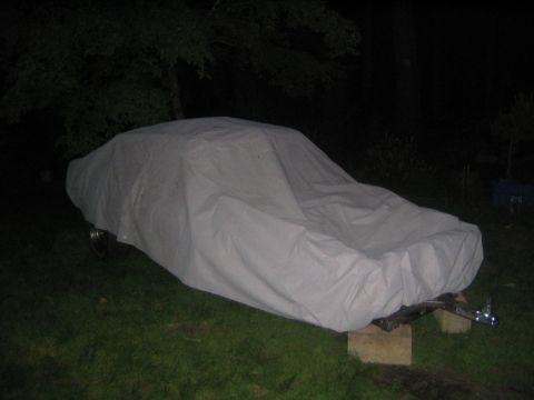 1978 Ford Bronco - Vehicle draped in a light gray fabric car cover, parked on grass at night with a flash exposure and dark woods behind. A tow bar or hitch a…