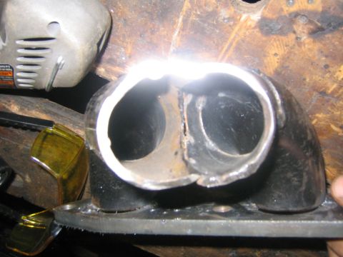 1978 Ford Bronco - Close-up of a cut-open exhaust or intake manifold flange on a workbench, showing two side-by-side port openings with freshly ground metal e…