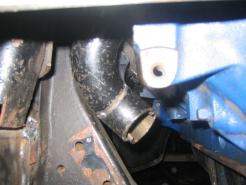 1978 Ford Bronco - A close-up view shows an exhaust pipe connected to a blue engine block, with visible rust on surrounding metal components.