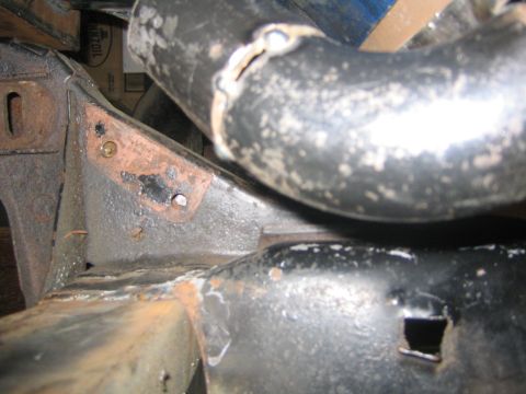 1978 Ford Bronco - Tight close-up of a rusted, black-coated frame bracket area with an axle tube curving through the frame, showing surface corrosion, weld be…