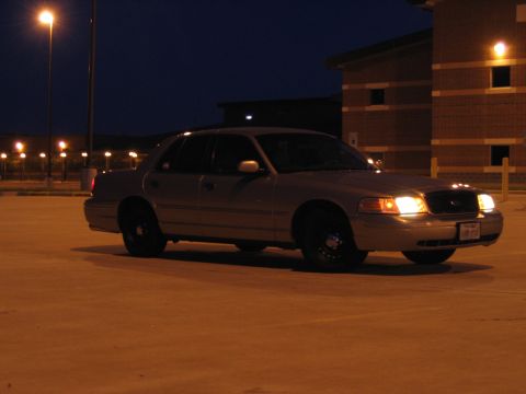 2000 Ford Crown Victoria - A silver sedan is parked in a lot at night, illuminated by streetlights and building lights.