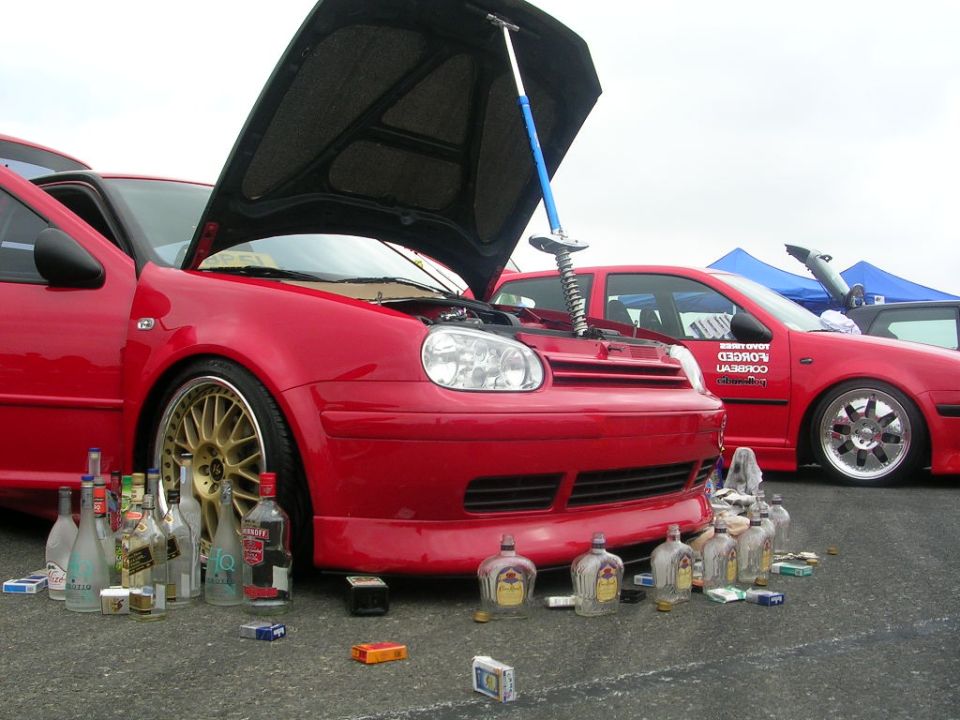 red Volkswagen Golf GTI with hood open, bottles and cigarette packs on ground