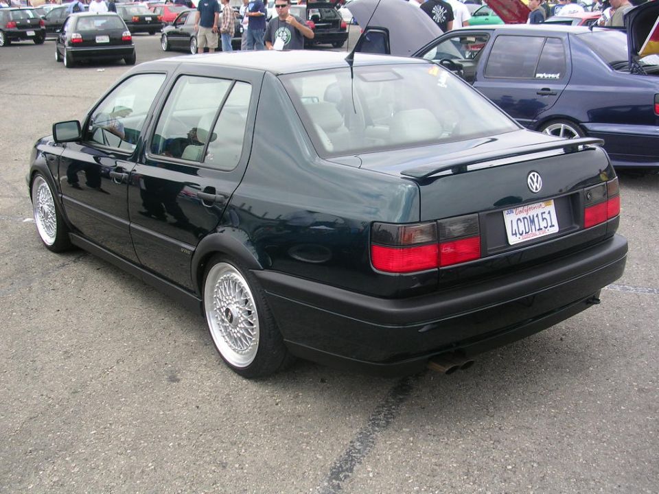 Dark green Volkswagen Jetta with aftermarket wheels and a rear spoiler, viewed from the rear
