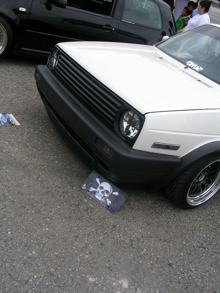 White VW Golf GTI parked next to a black car. Skull and crossbones sticker on the ground