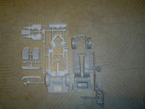 1979 Ford Bronco - Unassembled model kit parts for a vehicle chassis and engine are laid out on a patterned surface.