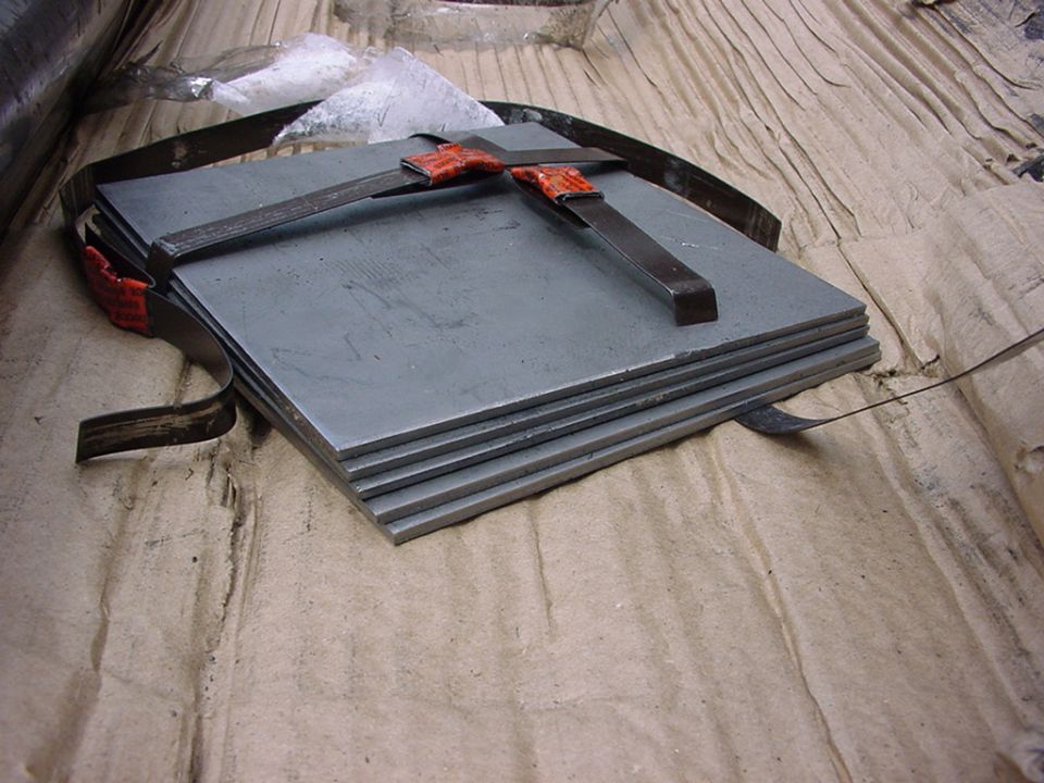 Stack of flat metal plates secured with straps and orange clamps