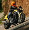 1985 Ford LTD Crown Victoria - Rider on a yellow motorcycle navigates a sharp curve on a mountain road.