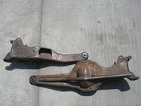 1990 Ford Bronco - Two rusty steel suspension components, likely control arms or axle brackets, laid on a concrete floor.