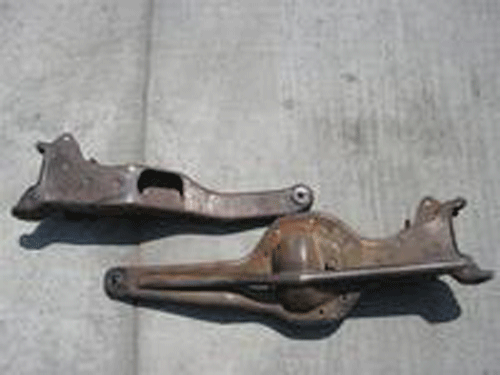 Two rusty steel suspension control arm or axle brackets on concrete